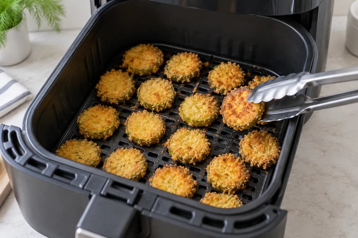 Golden pickle chips spaced in an air-fryer basket.