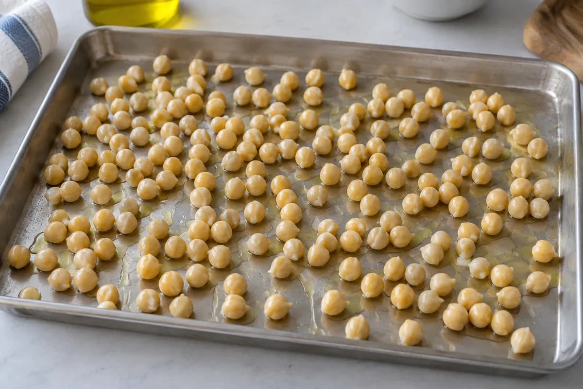 Oiled chickpeas spread in a single layer on a large roasting tray.
